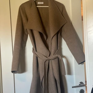 WERA kappa  - En kappa från Wera i nyskick använd ett par fåtal ggr. Nypris 1499kr. Säljer för 700kr. Mysigt material och i en fin beige/ljusbrun färg och med ett knytband runt midjan. Även två fickor. 