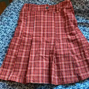 Orange kjol i fint rutigt mönster. Den är 54 cm lång och är 72cm runt hela midjan, den har både knapp och dragkedja<3