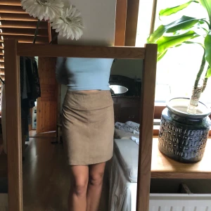 Beige kjol - Material: mocka. Sälja pga att den är för stor. Dragkedja där bak. Fint skick. Färgen syns bäst på bild 2. Frakt tillkommer.