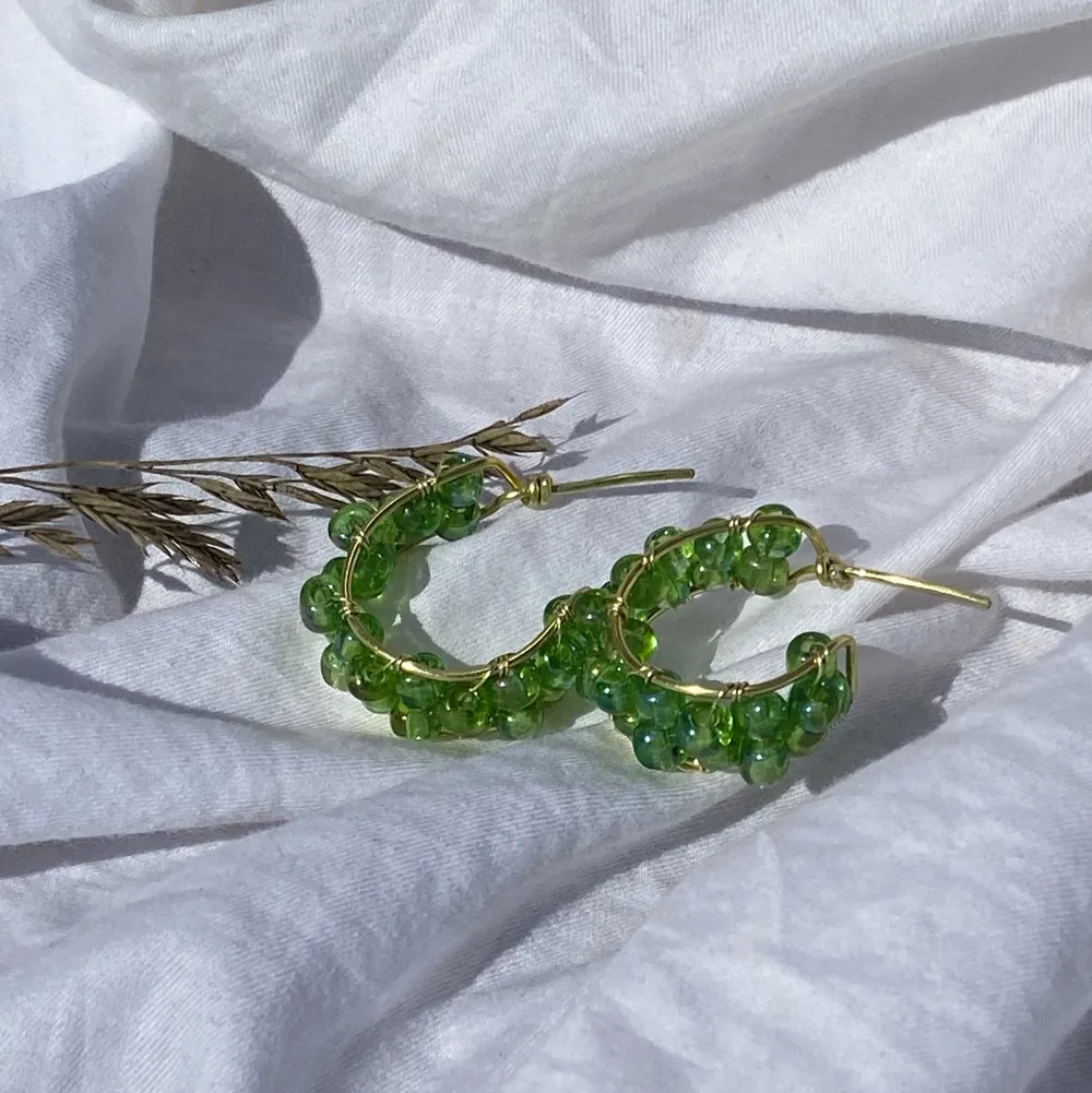 Handgjorda örhängen med gröna pärlor, och guldpläterad koppartråd. Nickel-, kadium-, och blyfria. OBS! Kommer utan plupp att sätta på baksidan.  2,5 cm i diameter. Accessoarer.