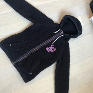 PeakPerformance Teddy fleece  - Det är en äldre peakperformance hoddie som inte längre går att köpa. Den är svart med vita och ros detaljer samt två dragkedjefickor. Jättebra skicka och har inte alls använts många gånger. 