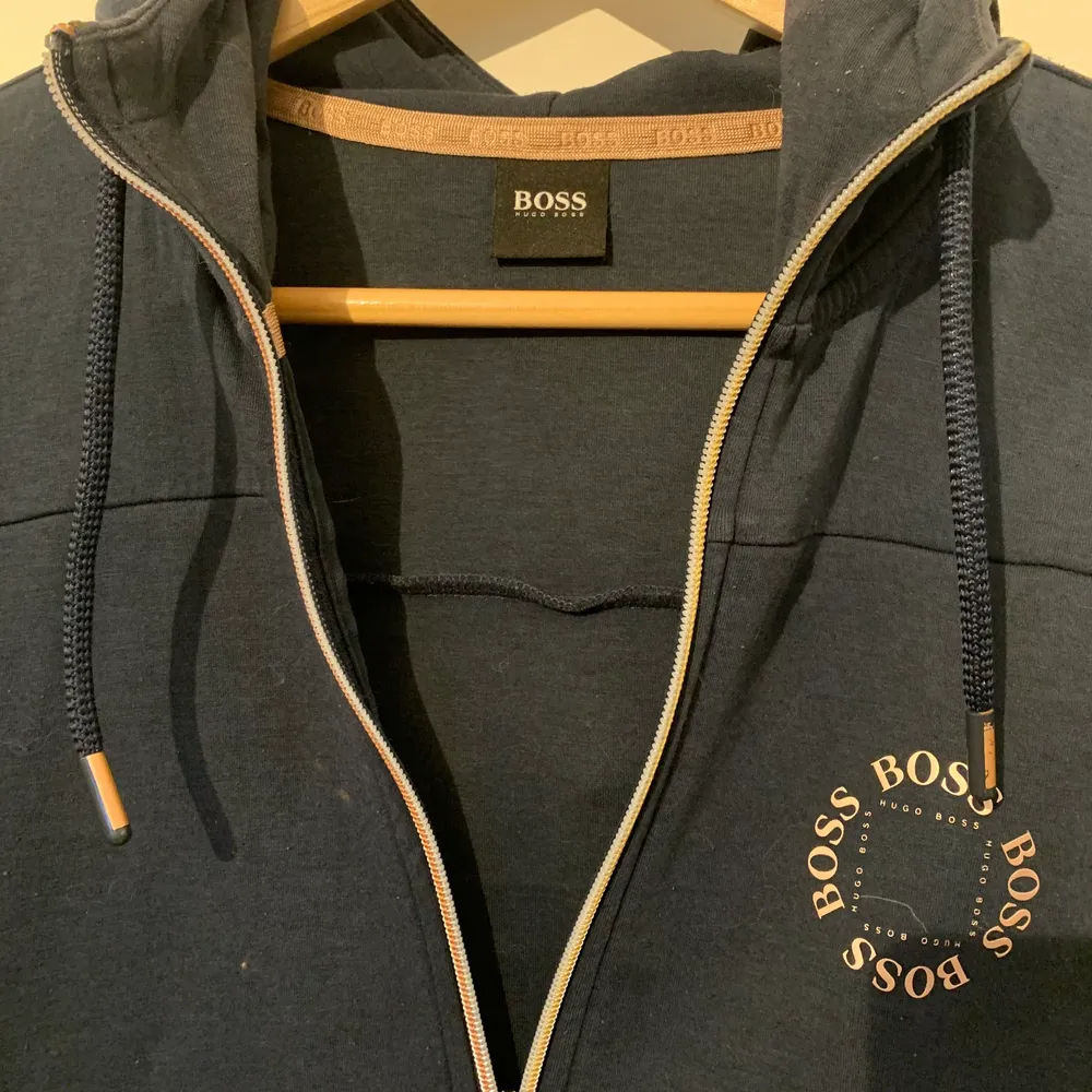 Marinblå Hugo Boos hoodie med guld/brons färgad dragkedja. Använd en del, däremot inga skador eller fläckar men små ”nopprar” på tyget finns. Går att få bort dock. Passar storlek M, Inge mer eller mindre. Bekvämt material invändigt. Nypris ungefär 1500kr.. Hoodies.