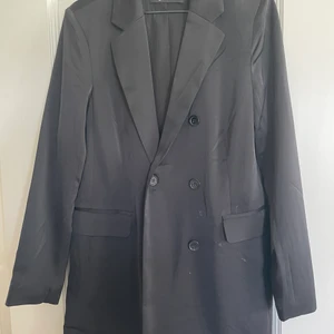 Kavaj från ginatricot  - Snygg kavaj den är lite längre men sitter snyggt! Mer i det glansiga materialet än matt. Är i bra skick men använd.