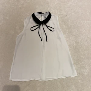 Vit blus med svarta detaljer. - En vit blus med fin svart krage och rosset. Syns lite igenom men det är inga problem, det går bra att ha ett vitt eller svart linne under.