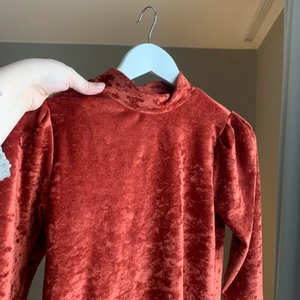 Roströd polo - Sammetliknande polo med små puffärmar/axelvaddar. Storlek S från Gina Tricot. Finns i Mölndal/Göteborg eller skickas med Postnord, köparen står för frakten.