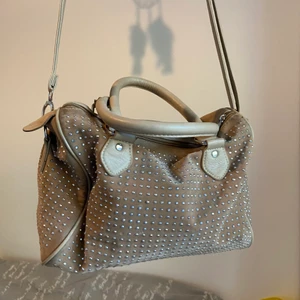 Snygg beige väska  - En Väsk som både går att ha som axel-och handväska, den har små silvriga ”nitar” på framsidan och mycket utrymme inuti🤎 OBS. Vill bara skriva att den har en defekt vid ena fästet på de långa ba det, den är dock lagad, men ska försöka fixa så att den ser ut som original! :))