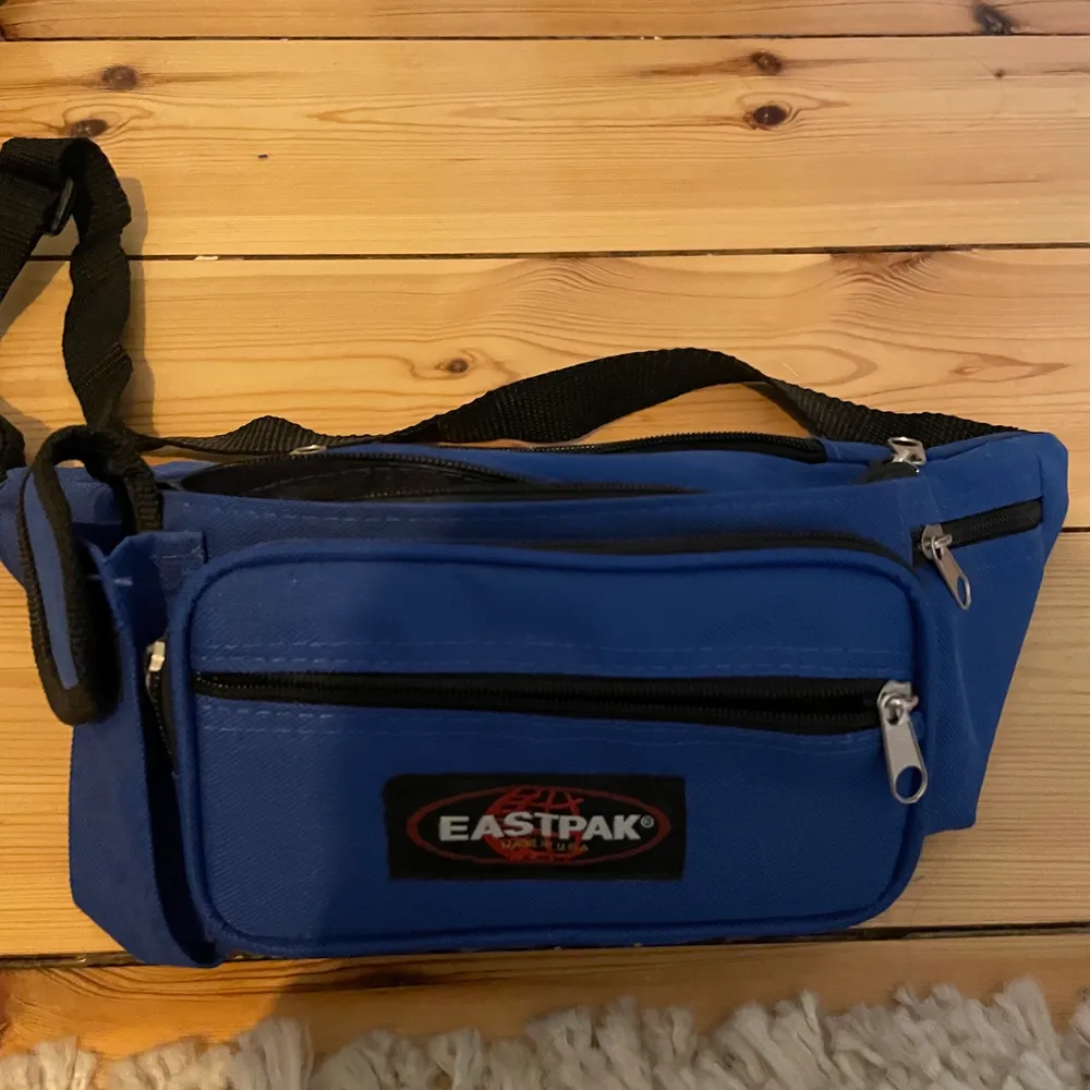 En eastpack midjeväska i blått och en svart väska med randigt axelband. Midjeväska från Utility innovation.. Väskor.