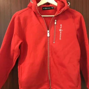 Sail Racing Bowman zip hoodie  - Jag säljer min röda Sail Racing hoodie då den är för liten. Har användt den väldigt sparsamt och få ggr. Det finns inga hål eller trasiga sömmar. Inga defekter. Där av så är tröjan i bra skick. Unik. Ny pris 1200 kr