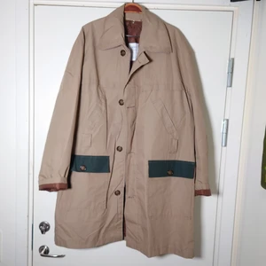 Vintagejacka - Beige vintagejacka, tunnt fodrad och med stora fickor! Mörkgröna detaljer och brunt foder. Kan stängas med dragkedja och knappar. Stor och härlig oversize, går ner till knäna på mig som är 164cm lång. 