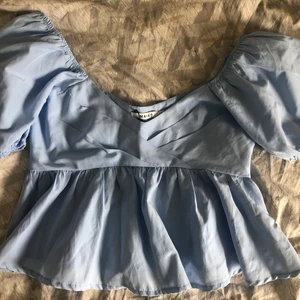 Ljusblå topp med volang NA-KD - Ljusblå topp med volang från NA-KD. Säljer då den inte passar mig. Jag har testat den en gång. Köptes 2020 och har bara legat i garderoben och skräpat. Prislappen sitter kvar. Toppen har en dragkedja på vänster sida som går från armhålan ner till slutet av volangen. Den är liten i storlek så den passar en 36. Nypris är 400kr.