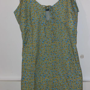 Sommar Klänning  - En superfin oanvänd blå och gul blommig klänning i ett tunt material. Den är endast testad och säljs för att den inte passade. Den har en lång dragkedja på ryggen