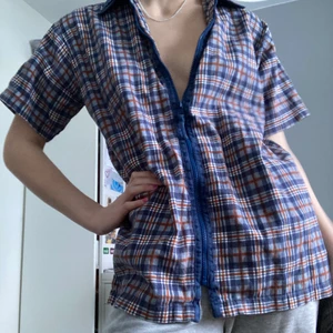 Kortärmad skjorta  - Kortärmad skjorta med dragkedja(!) i rutigt Manchester-tyg!! Blåa detaljer runt dragkedjan och kragen. Går att ha som den är eller över en annan tröja. Barnstorlek men sitter oversize på mig som har xs/s 