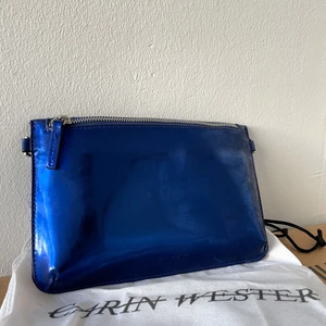 Carin Wester väska  - Metallblå kuvertväska från Carin Wester. Aldrig använd. Kommer med dustbag och matchande band. Kan mötas upp i Malmö, vid köp ingår frakt!
