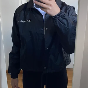 CHAMPION Vindjacka - Svart vindjacka från Champion som endast är använd enstaka gång. Kanon skick! Strl L, men sitter lite löst på mig som är S. Broderade loggor. Köparen står för frakt