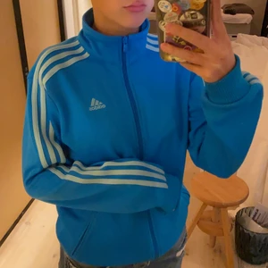 Blå/turkos adidaströja/jacka - Sportig adidas tröja som även funkar som jacka och till vardags. Säljer pga inte min stil/kommer inte till användning. Fint skick förutom två små svarta fläckar (skulle tro det är från ngn penna, se bild 3). Köpt på second hand men ej använd mkt. Två fickor som rymmer hyfsat mkt. Storleken är L men sitter ganska perfekt på mig som är en XS/S (se bild 1&2). Material: 85%polyester och 15% bomull. Vid intresse/fler frågor/bilder skriv till mig under annonsen (kontakta). Avhämtning på Södermalm eller frakt till självkostnadspris (bestäm själv om du vill ha spårbart eller ej)<3:)