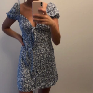 Småblommig klänning  - Blå klänning med vita blommor med rosett som man kan dra åt och knyta över bysten. Storlek M men passar även S bra! Använd 1 gång så i bra skick. 