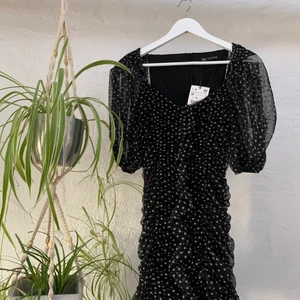 Svartklännig - Super snygg svart klänning i ett vit-prickigt mönster. Perfekt till utgång eller festligare tillfälle. Oanvänd i strl M från Zara. Klänningen är smockad som ni ser på bild 1 och har mesh-liknande ballongärmar. Kan bäras som på bilden eller off-shoulder🖤