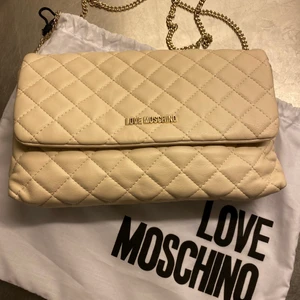 Love Moschino quiltad väska - Love Moschino i mjukt cremevitt skinn. Använd vid ett tillfälle och inköpt på Åhléns city i Sthlm. Har tyvärr inte kvittot kvar. Kommer med dustbag.