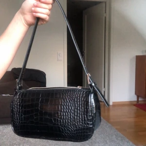 Glansig Svart väska - Svart glansig mini väska med silvrig dragkedja. Den är använd men har inga fel, missfärgningar eller trasiga delar. Passar till allt och är väldigt lätt och får plats med mycket saker. Den har även ett innerfack inuti vilket kan vara användbart.