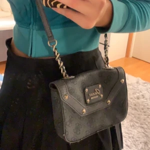  Guess väska - Cool lite mindre mörkgrå Guess väska! Den har fina detaljer som nitar och leopardmönster inuti, samt en innerficka. 
