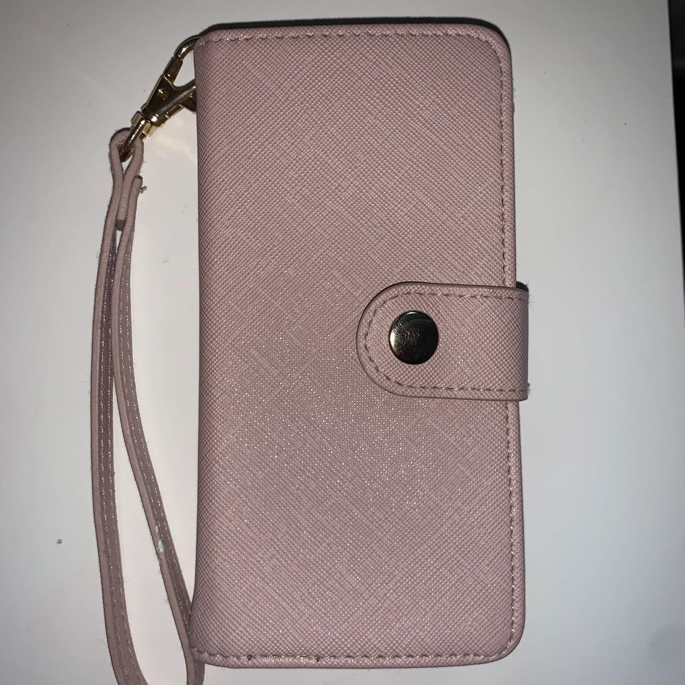 Ett rosa plånboksskal med korthållare i och sedelhållare. Man sätter på mobilen genom att dra i kanterna på svarta delen och sätter på mobilen. När man ska ta bild men bakkamera så trycker man bara upp den svarta delen medans mobilen fortfarande sitter på. Skalet har också ett band som man kan stoppa igenom handen. Skalet är runt 2 år gammalt. . Övrigt.