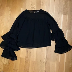 Svart blus, Storlek XS - Aldrig använd. Köpt från bikbok i storlek XS. Volanger vid skärmarna. Mer synlig över brösten. Knapp på baksidan som går att knäppa upp. 