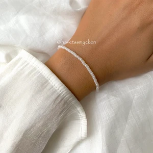 Skimrande pärlarmband  - Pärlarmband av skimrande glaspärlor i vit nyans. Perfekt att kombinera med andra smycken! Armbandet är ihopsatt med hållbar elastisk tråd och passar de flesta handleder.