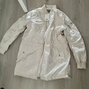 OANVÄND MÄRKES JACKA  - lång jacka i storlek M. Beige vit i tonen. Oanvänd 