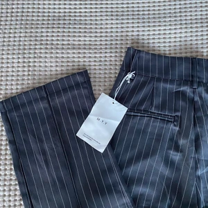 Randiga, grå kostymbyxor - Oanvända randiga kostymbyxor, men har tyvärr några lösa trådar. Vikningar längs benen. Listad storlek när jag köpte dem var L, men de var alldeles för små på mig som i vanliga fall har M. Midjemåttet är cirka 70 cm och längden (inseam) är 65 cm vilket normalt är storlek S. Köpare står för frakt. 