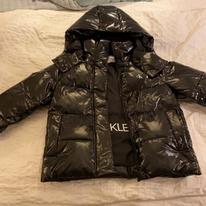 Glansig vinterjacka  - Jag säljer min trendiga, glansiga vinterjacka från Calvin Klein! Den är helt oanvänd med prislappen kvar. Säljer pågrund av felköp. Det är en varm fodrad jacka med luva som man även kan dra av. Kvitto finns💕