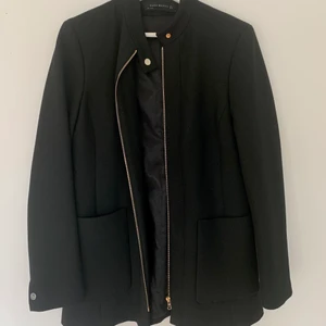 Svart jacka från Zara/ stl: M/ nyskick - Figursydd jacka i nyskick från Zara i storlek M. Endast testad. Säljes då den bara blivit hängandes i garderoben. Jackan har två fickor framtill samt stängs med dragkedja i guld. Nypris 800 kronor. Färg: svart.