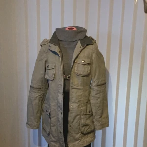 Hurricane coat - Hurricane coat färg grön. Fodret är grått.  Längd 83 cm, ärmlängd 65 cm, mått från ärm till ärm 39 cm. 