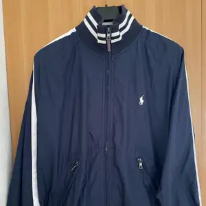 Polo Ralph Lauren jacka i track top liknande modell med nylon i yttermaterialet och mjukt innerfoder. Perfekt vår/sommarjacka i strl L men passar M på längden då modellen är kort. Väldigt sparsamt använd, 9/10. Inköpt i New York på Macys för cirka 3.000 kr. 