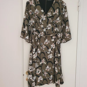 Klänning från MQ - Khakigrön klänning i chiffong med blommor i beige/svart/vitt. Den har 3/4 långa klockärmar och går till knät. Dold dragkedja i ryggen. Superfin fit som passar de flesta kroppsform sitter som en stl.34 ska. Band knyts bak eller fram, vad man tycker är snyggast. I nyskick och inga fläckar eller märken. Använd 1 gång.  (Kan säljas för 150kr om man möts upp i jkpg innan 15e augusti.)