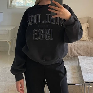 Mörk grå/svart Gina tricot tröja.  - Säljer denna fina tröjan med blå text ”ATHL.DEPT AMERICA 1983” inramat med vitt eftersom att jag inte använder den längre. Är som ny och väldigt skön. 🥰 