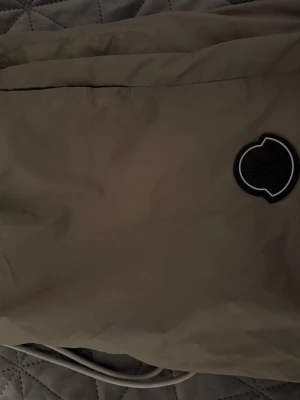 Beige badbyxor från Moncler - Snygga beige badbyxor från Moncler med vit dragsko och metalländar. Klassisk Moncler-logga på ena sidan och diskret tryckt varumärke nedtill. Perfekta för stranden eller poolen. Storlek L passar M