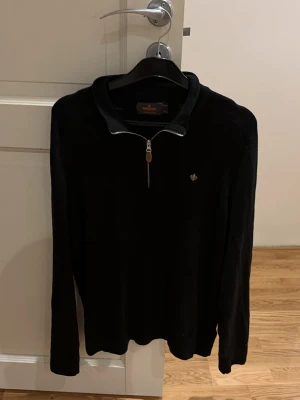 Svart halvzip tröja från Morris - Stilren svart tröja från Morris med halvzip och liten logga broderad på bröstet. Tröjan har krage i kontrastmaterial och långa ärmar. Perfekt för en avslappnad men snygg look. Passar storlek M men också S.