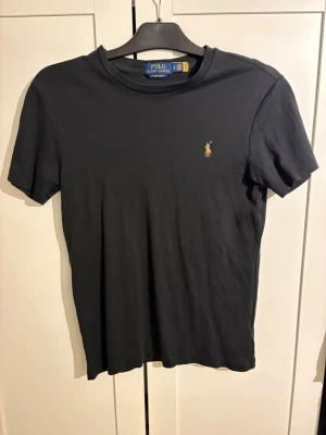 Svart t-shirt från Polo Ralph Lauren - Svart t-shirt från Polo Ralph Lauren i modellen Custom Slim Fit. Klassisk design med korta ärmar och liten broderad logga på bröstet. Tillverkad i mjuk bomull som känns skön mot huden.