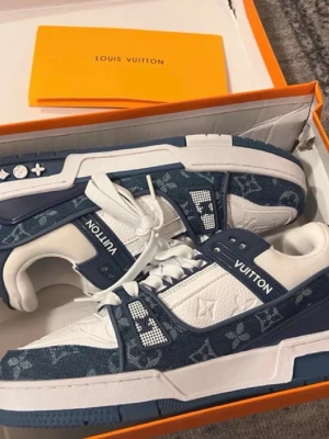 Louis Vuitton blå/vita sneakers - Säljer ett par Louis Vuitton sneakers i blått och vitt med klassiskt monogrammönster. Skorna har snörning, platt sula och detaljer i både skinn och textil. Snygg kontrast mellan marinblå och vita partier samt tydlig LV-logga på sidan och sulan. (Lådan kommer inte med pågrund av att den har gått sönder.