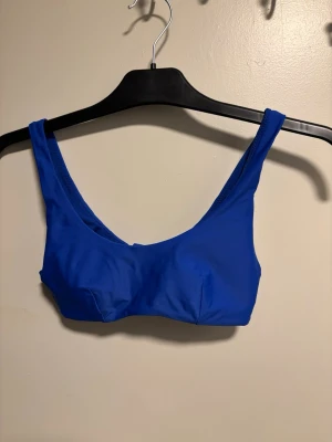 Kornblå bikiniöverdel med breda band - Snygg kornblå bikiniöverdel med breda axelband och enkel, sportig design. Modellen har rundad urringning och spänne i ryggen. Tillverkad i stretchigt material som passar perfekt för strand eller poolhäng.