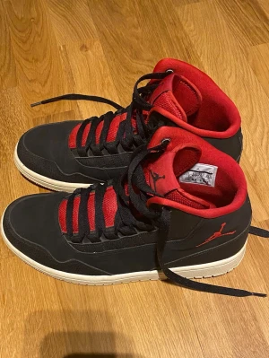  Nike Air Jordan 1 High - Säljer ett par snygga Nike Air Jordan 1 High sneakers i svart och rött med klassisk Jumpman-logga på plösen och sidan. Perfekta för dig som gillar streetwear och ikonisk sneakerstil.Svart/röda snöre medföljer.