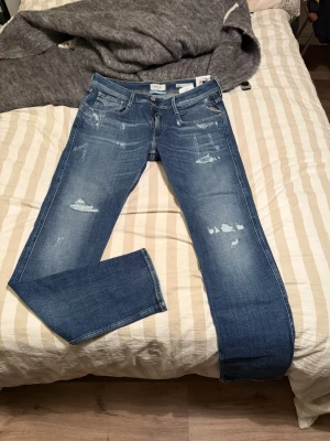Blå slitna jeans från Replay - Snygga blå jeans från Replay med slitna detaljer och klassisk femficksmodell. Jeansen har normal passform. Perfekta för en avslappnad och trendig stil. Oanvända pga av för små. 1200 lägsta pris 