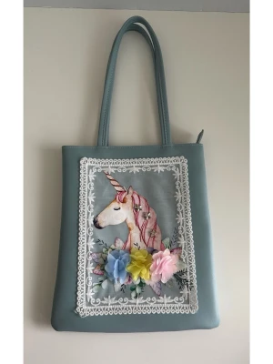 Blå handväska med enhörning och blommor - Söt ljusblå handväska med långa handtag, dekorerad med en broderad enhörning och färgglada 3D-blommor framtill. Väskan har vita spetsdetaljer runt motivet och är tillverkad i syntetmaterial. Perfekt för dig som gillar unika accessoarer med fantasifull touch. Helt NY!!