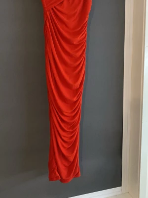 Röd långklänning från SHEIN - Snygg röd långklänning från SHEIN med draperad effekt längs hela klänningen. Klänningen har en figurnära passform och är tillverkad i ett mjukt syntetmaterial som ger ett elegant fall. Perfekt för dig som vill sticka ut med en färgstark look.