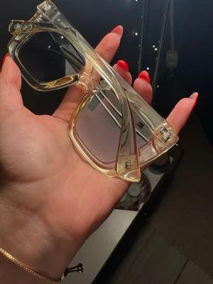 Transparenta fyrkantiga solglasögon juicy couture - Säljer ett par trendiga solglasögon med transparent, ljusgul plastbåge och stora fyrkantiga glas. Glasen är lätt tonade och ger en cool retrovibe. Perfekta för dig som vill sticka ut med en unik accessoar.