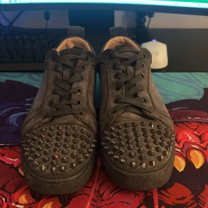 Mörkgrå mockasneakers med nitar - Unika sneakers i mörkgrå mocka med coola nitar över tån. Skorna har snörning och platt sula, samt beige insida. Perfekta för dig som vill sticka ut med en edgy stil. Passar till både streetwear och mer avslappnade outfits.