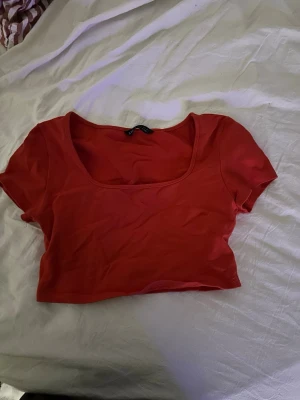 Röd croppad topp med kort ärm - Trendig röd croppad topp med korta ärmar och fyrkantig ringning. Perfekt att styla med låga jeans eller kjol för en cool look. Mjuk och stretchig känsla, passar dig som gillar en enkel men snygg stil.