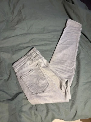 Ljusgrå slim fit jeans från Replay - Snygga ljusgrå jeans från Replay i slim fit-modell. Jeansen har klassisk femficksdesign, bälteshällor och subtila slitningar för en trendig look. Perfekta för dig som gillar en smal passform och stilren färg. Billigare vid snabb affär 