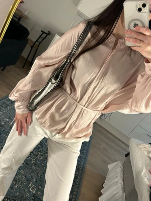 Ljusrosa sidenblus från STOCKH LM - Supersnygg ljusrosa blus i glansigt siden från stockh lm. Blusen har långa, puffiga ärmar med breda manschetter och en avslappnad passform. Perfekt till både jeans och kostymbyxor för en chic look.