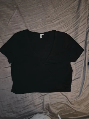 Svart croppad omlottopp H&M - Snygg svart croppad omlottopp från H&M med korta ärmar och djup V-ringning. Tillverkad i mjukt bomullsmaterial som känns bekvämt mot huden. Perfekt till jeans eller kjol för en trendig look.